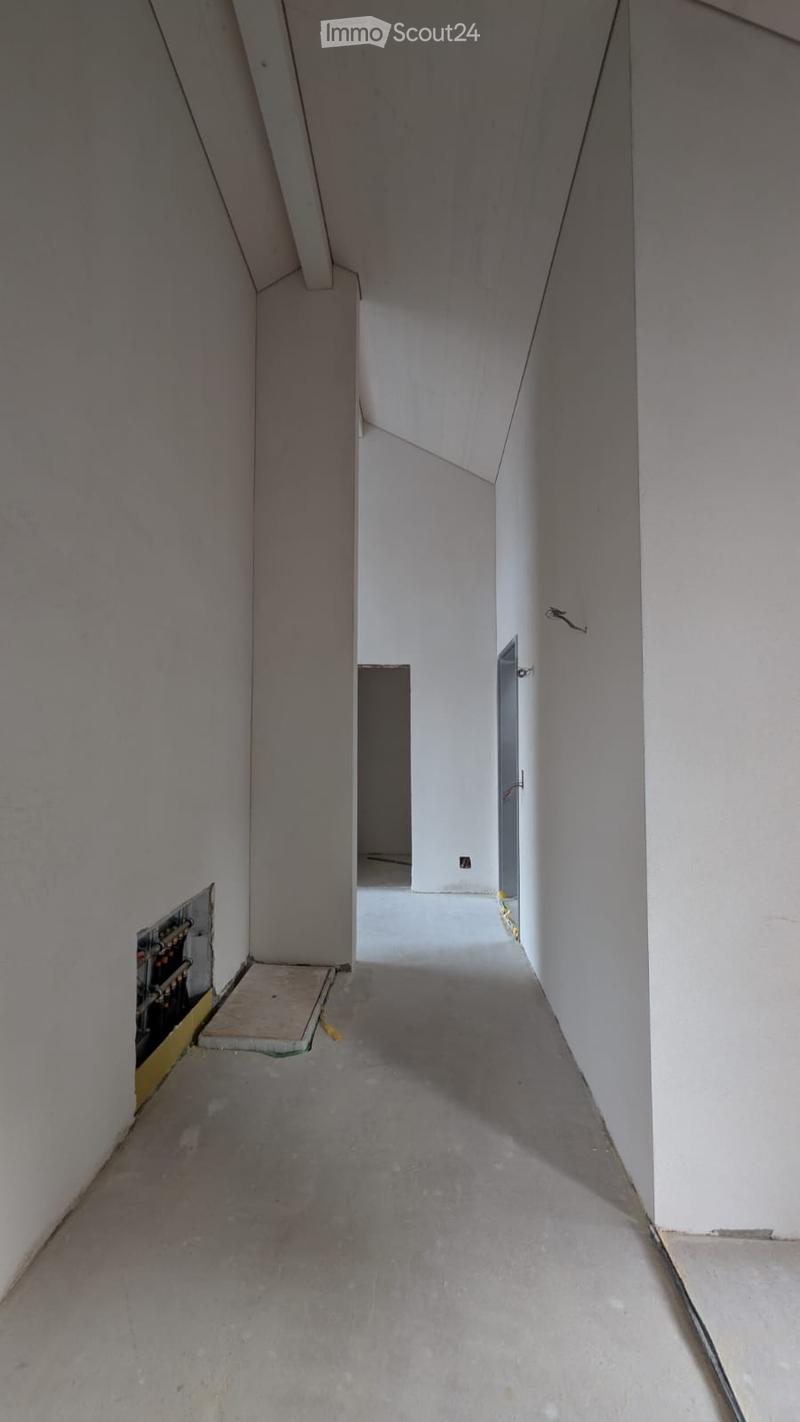 Empty hallway with white walls, concrete floor, and visible electrical panel on one side.
