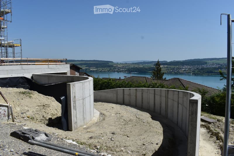 Construction site with concrete barriers, sand, and a view of a lake and distant hills.