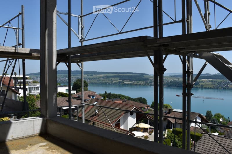 Balcony overlooking a scenic lake with surrounding houses and greenery.