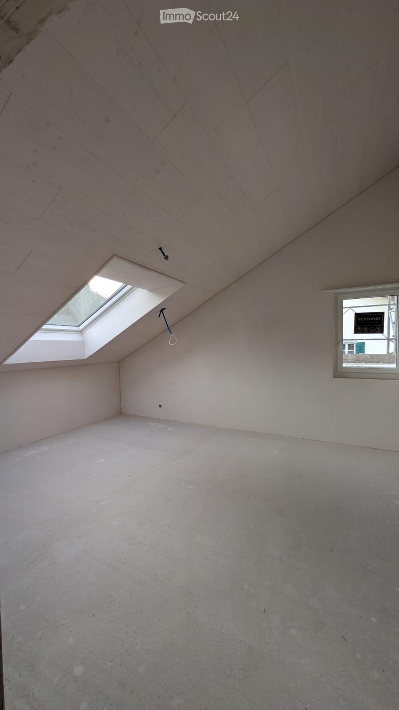 Empty attic space with wooden slanted ceiling, concrete floor, skylight window, and side window with a sign visible.