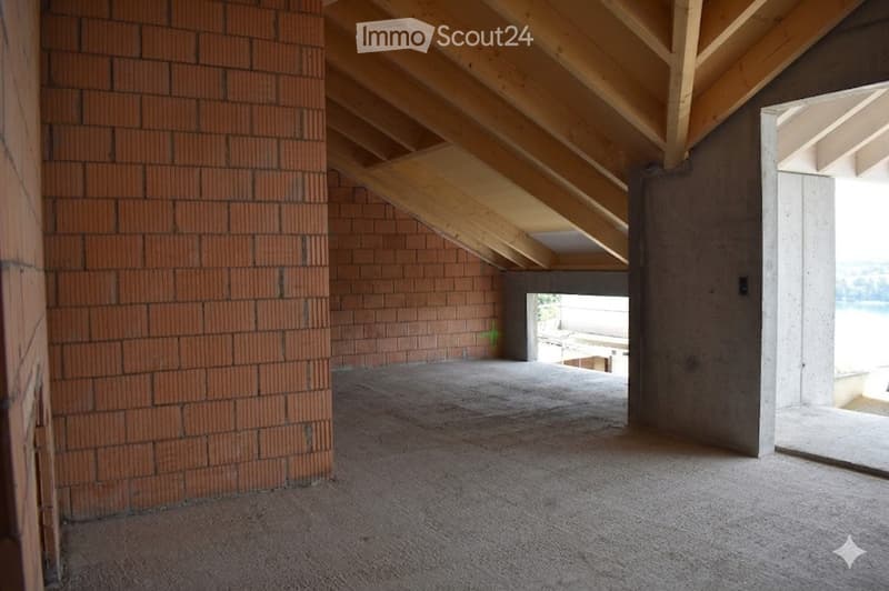 Empty room with exposed wooden beams, brick walls, and concrete floor. No furniture or equipment present.