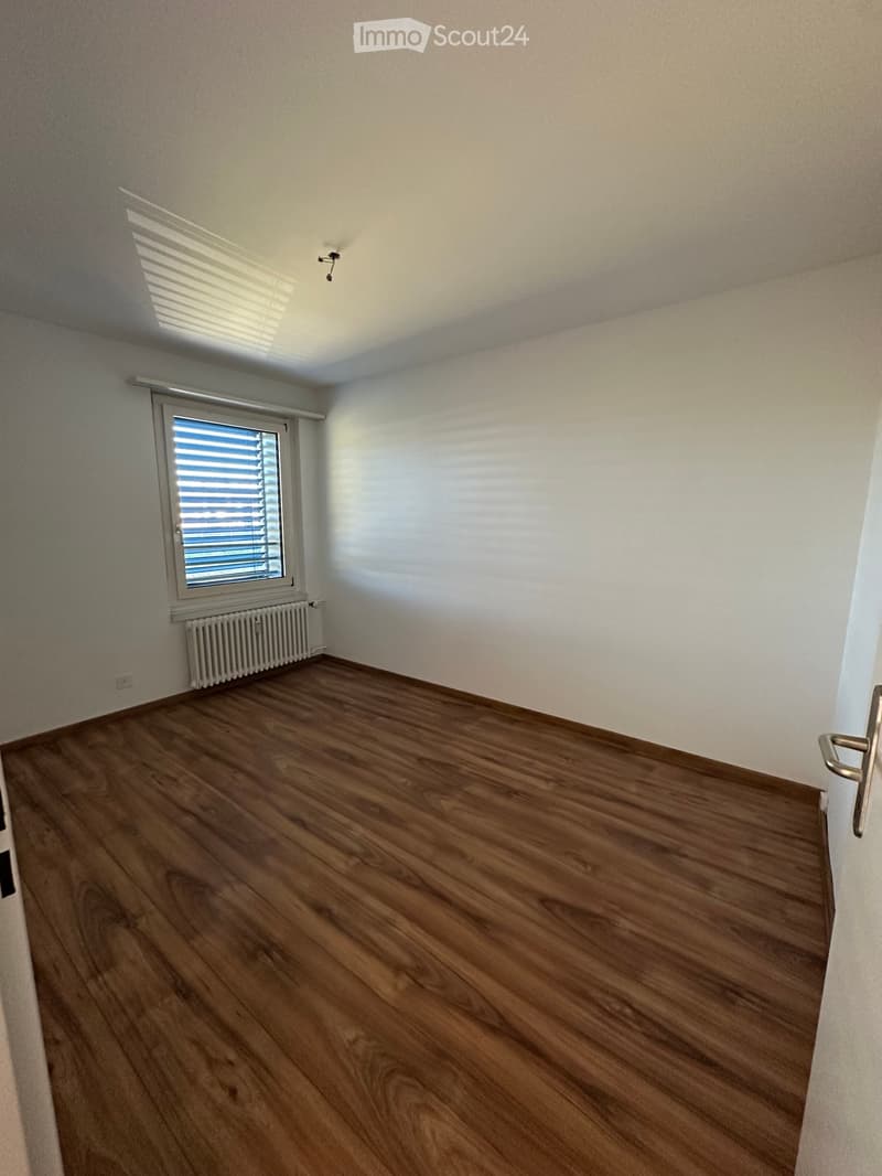 Empty room with wooden flooring, white walls, and a window with blinds. A radiator is visible below the window.