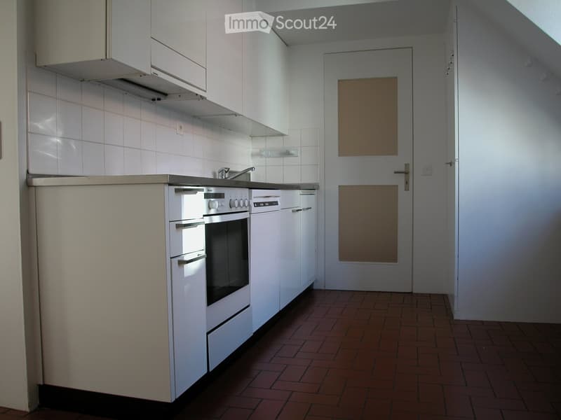 Compact kitchen with white cabinets, tiled walls, and a brick floor. Features an oven, dishwasher, and a faucet on the countertop.