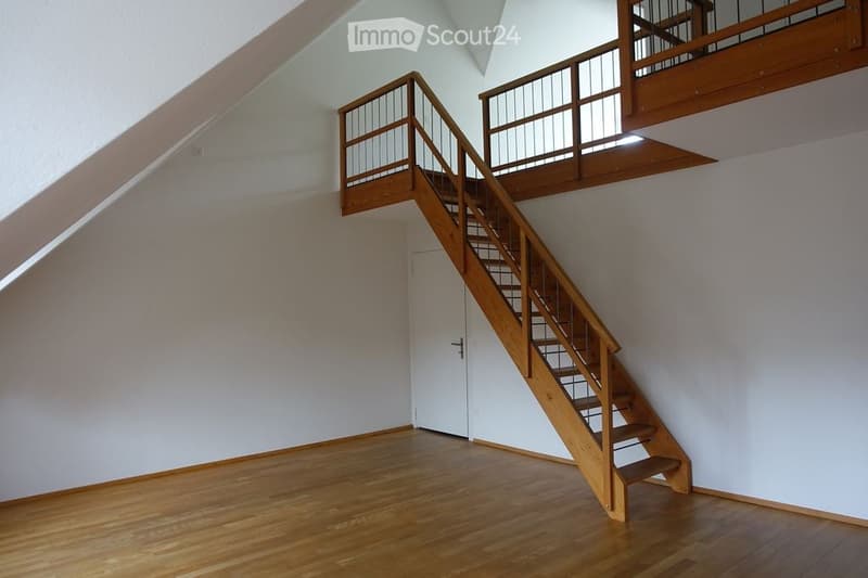 Empty room with wooden flooring, white walls, and a wooden staircase leading to an upper level. No furniture or equipment present.