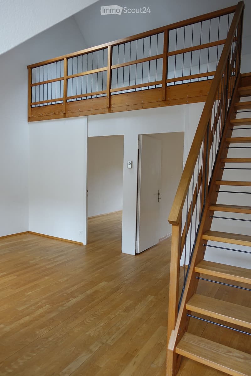 Empty hallway with wooden flooring, white walls, and a staircase leading to an upper level with a wooden railing and metal balusters.