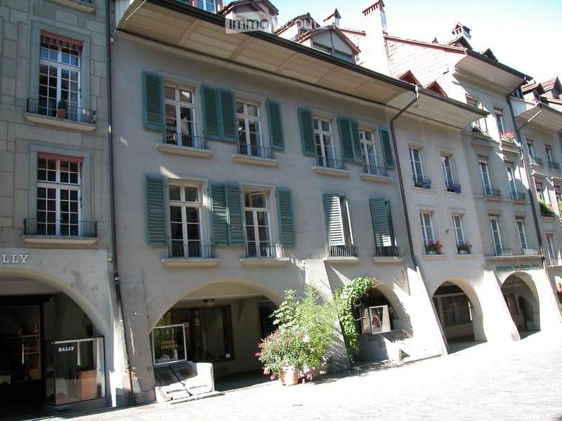 Multi-story building with classic European architecture, featuring arched entrances, balconies, shutters, and decorative elements.