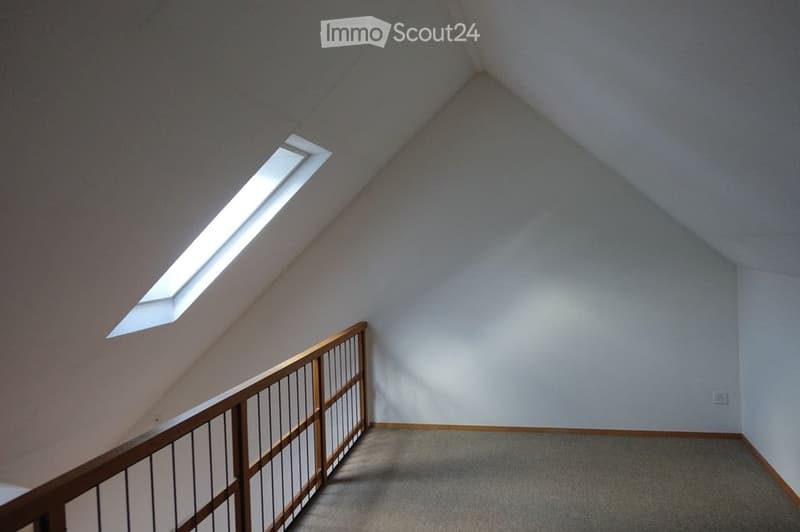 Empty attic space with sloped ceilings, wooden railing, and skylight window allowing natural light.