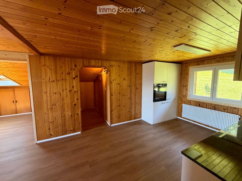 Bright, wooden-paneled kitchen with white cabinets, an oven, and large windows offering a view of the outdoors.