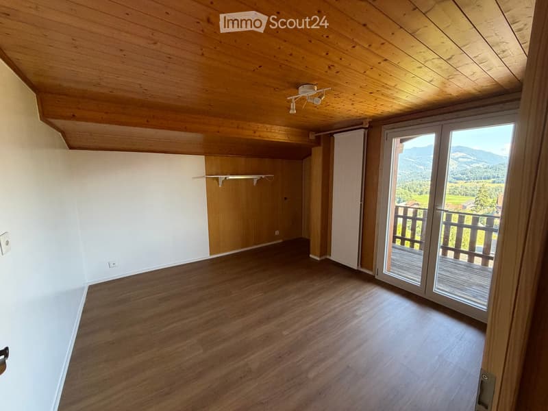 Empty room with wooden flooring, white walls, and a wooden ceiling. Features a sliding glass door leading to a balcony with a scenic mountain view.
