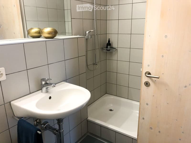 Modern bathroom with a white sink, bathtub, and tiled walls. Features a mirror with decorative spheres on the windowsill and a towel hanging on the side.