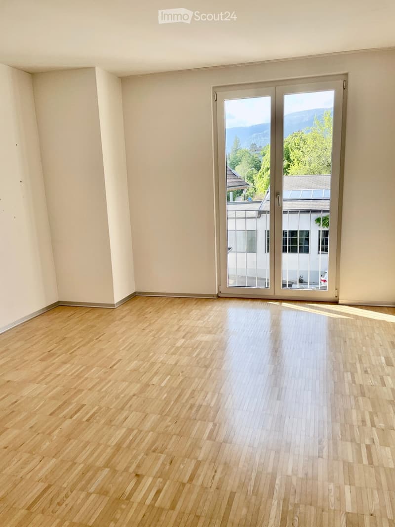 Empty room with wooden flooring and large sliding glass doors leading to a balcony with a scenic mountain view.
