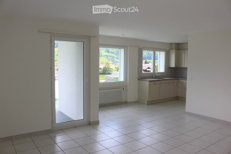 Empty kitchen with tiled floor, white walls, built-in cabinets, sink, and windows overlooking a green landscape.
