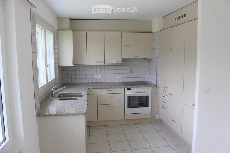Modern kitchen with light wood cabinets, granite countertop, double sink, and built-in oven.
