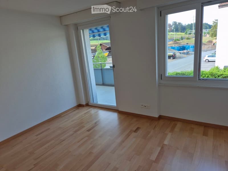 Empty room with wooden flooring, large windows, and a sliding glass door leading to a balcony.