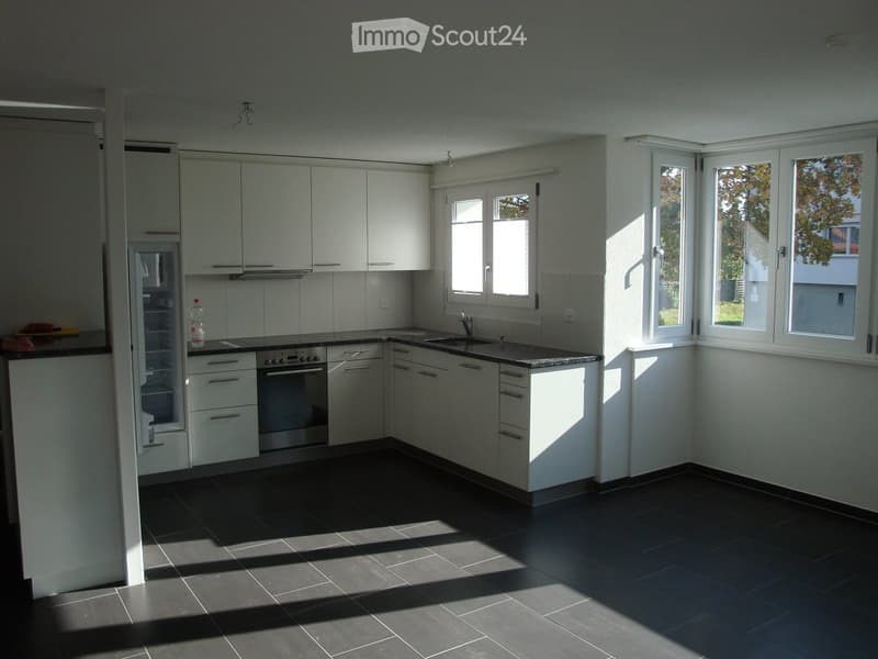 Modern kitchen with white cabinets, black countertops, and dark tiled flooring. Features a refrigerator, oven, sink, and faucet.