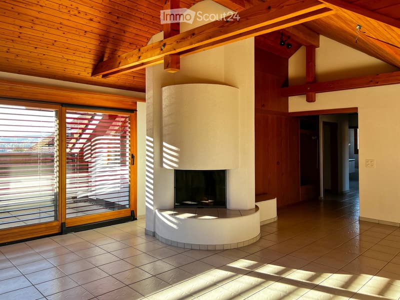 Living room with a central fireplace, wooden ceiling beams, large sliding glass doors with blinds, and tiled flooring.