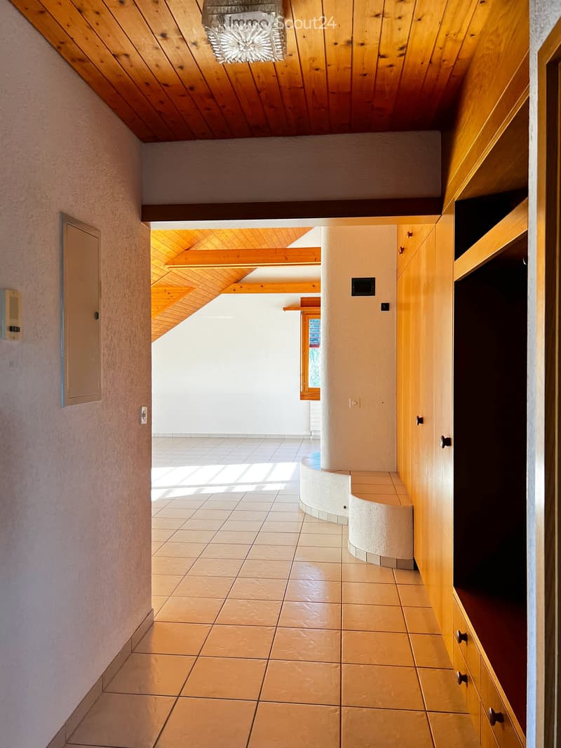 Spacious hallway with wooden ceiling beams, tiled floor, built-in wooden cabinetry, and a curved wall section.