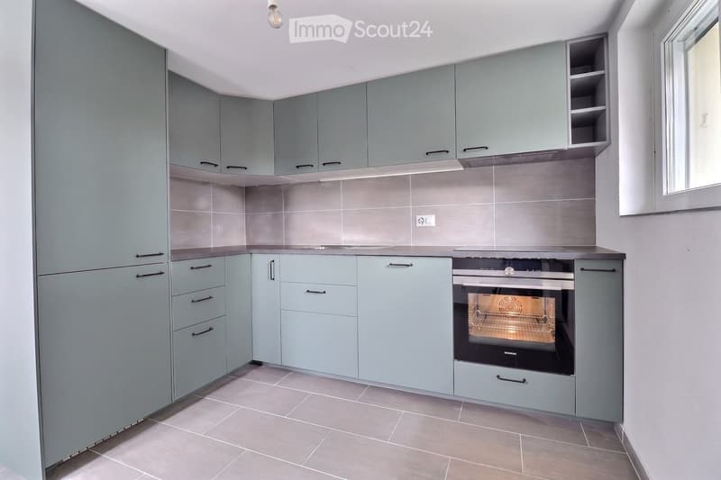 Modern kitchen with light blue cabinets, stainless steel oven, and tiled backsplash.