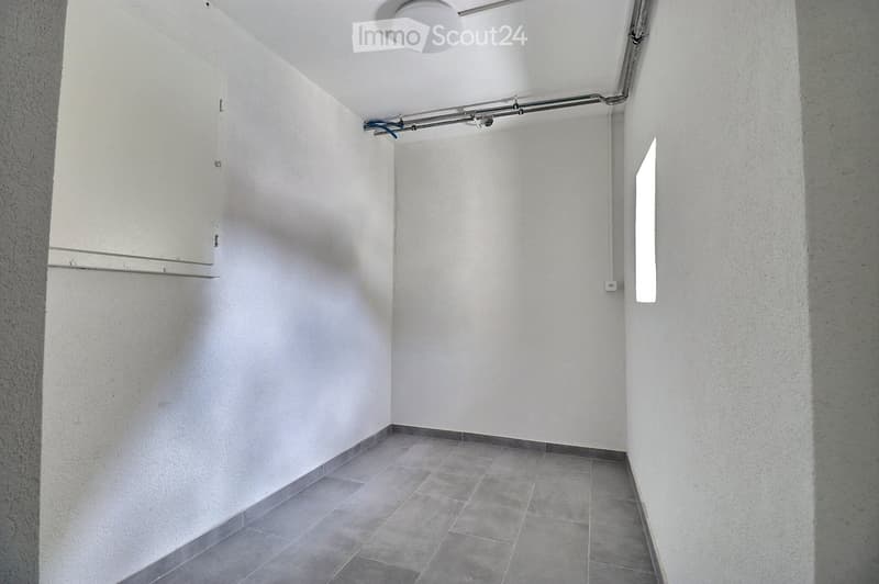 Empty hallway with white walls, tiled floor, and a small window allowing natural light.