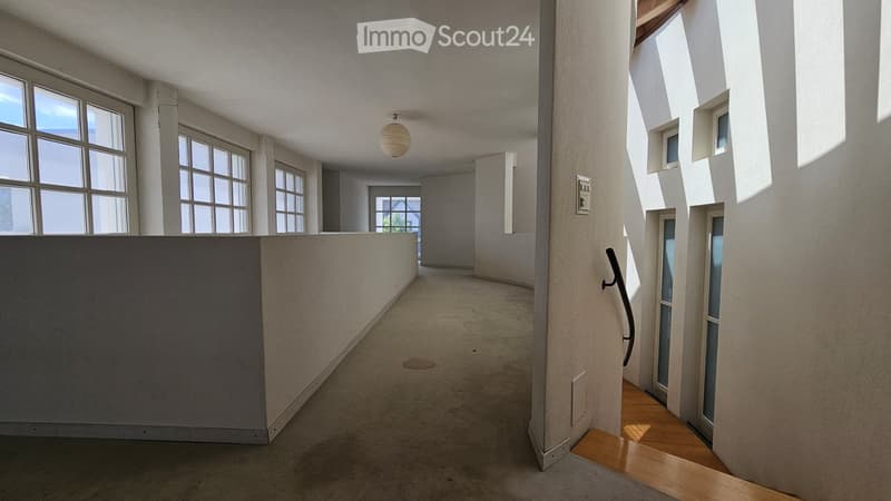 Bright, minimalist hallway with large windows, concrete floor, white walls, and a hanging light fixture.