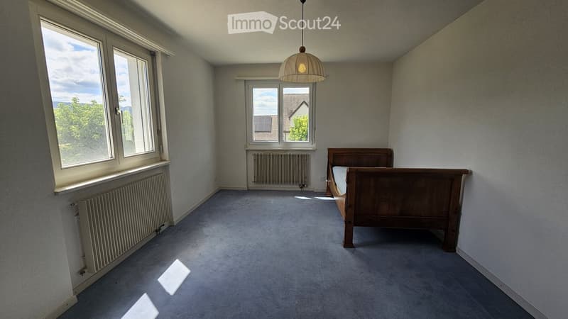 Spacious bedroom with large windows, wooden bed, and carpeted floor.