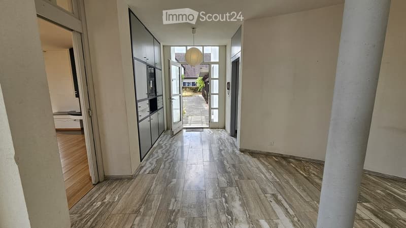 Empty hallway with polished marble flooring, white walls, and a hanging spherical light fixture. Open doors lead to adjacent rooms and an outdoor area.