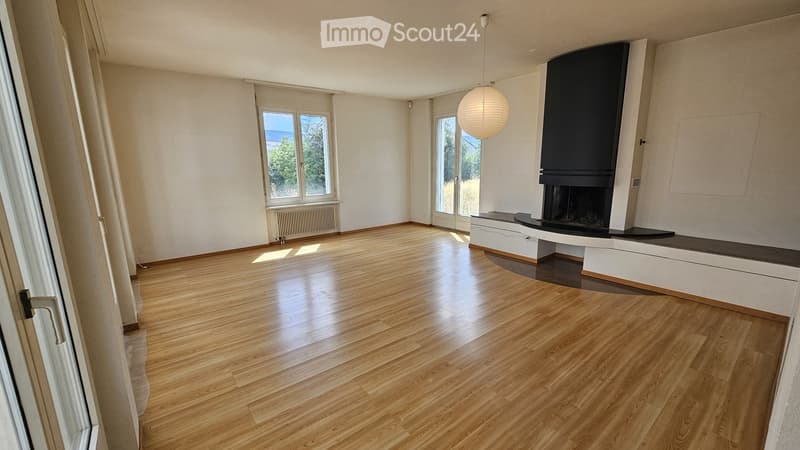 Empty room with wooden flooring, large windows, and a modern fireplace with a built-in seating area.
