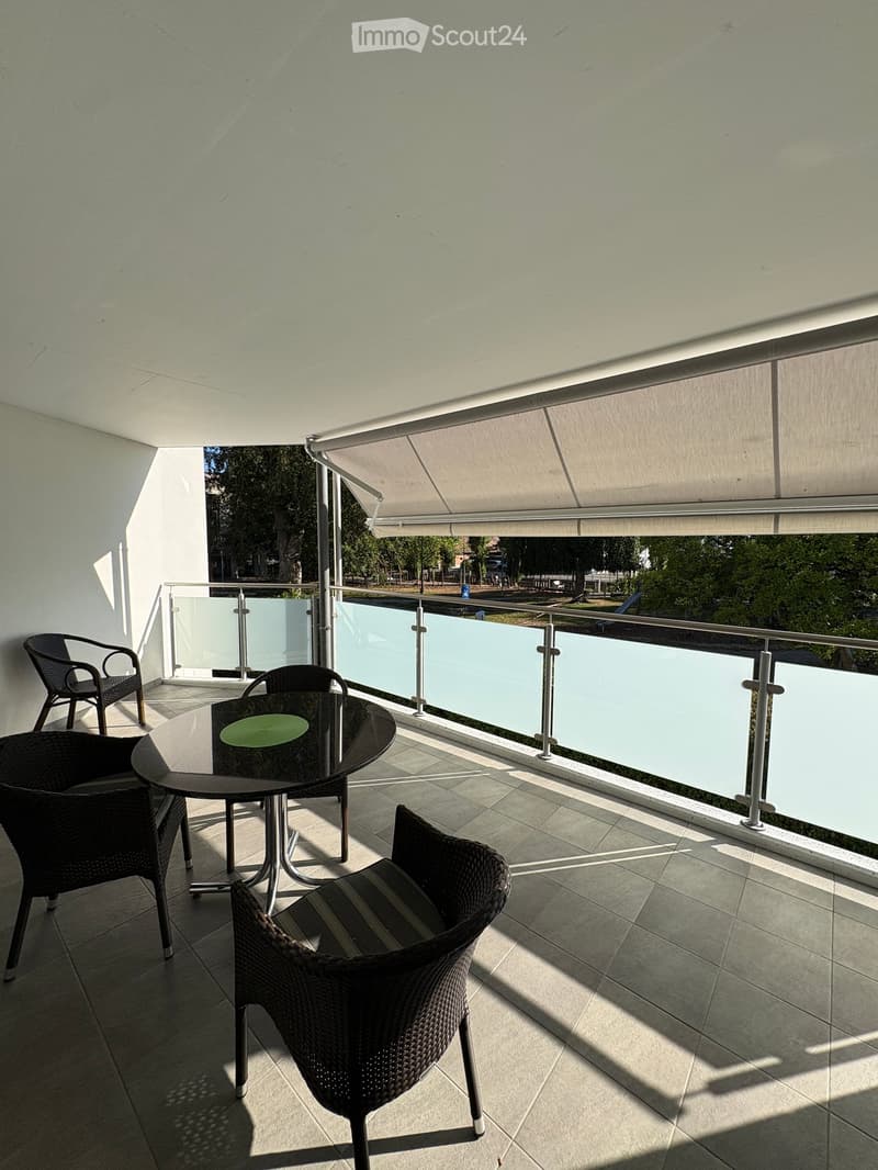 Balcony with a table and four wicker chairs, glass railing, and retractable awning.