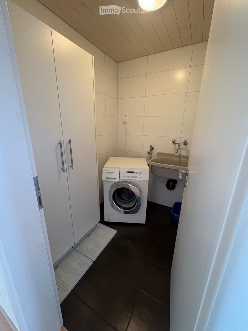 Compact bathroom with a white washing machine, a sink with a faucet, and white tiled walls.