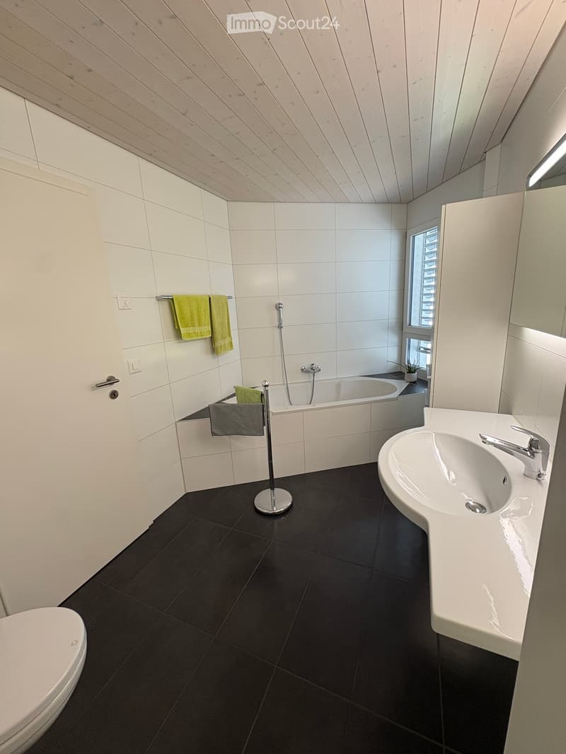 Modern bathroom with white tiles, black floor tiles, a white sink with a chrome faucet, a toilet, a bathtub, and a towel rack with towels.