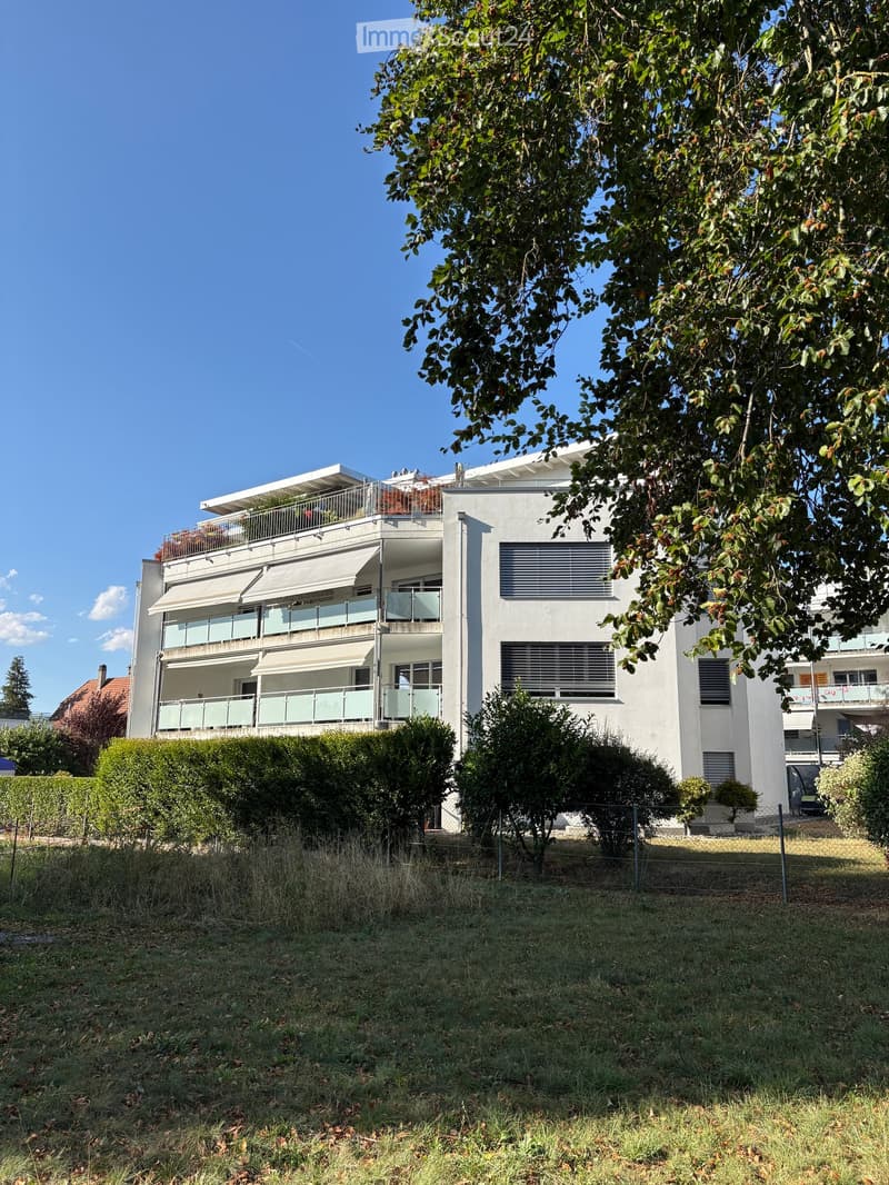 Modern two-story white building with balconies, large windows, and a tree in front.
