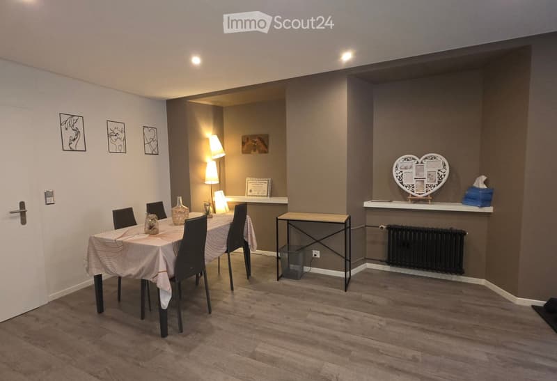 Dining area with a wooden table, chairs, vase, lamp, radiator, heart-shaped wall decoration, and picture frame.