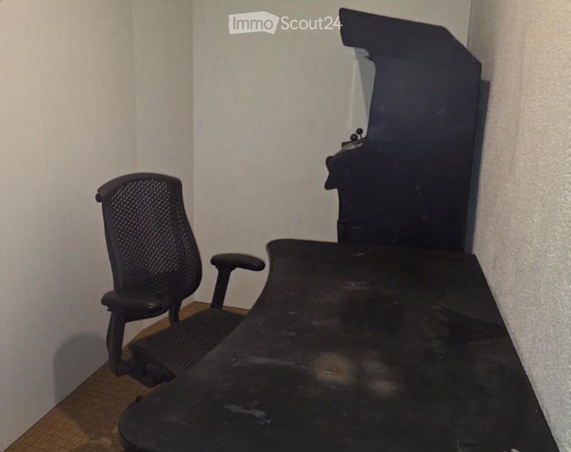 Office space with a black office chair and a black desk against a plain wall.