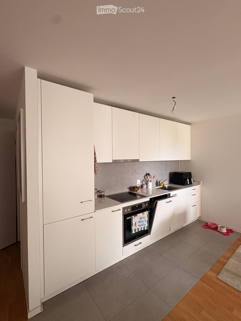 Modern kitchen with white cabinets, stainless steel appliances, and grey tiled floor.