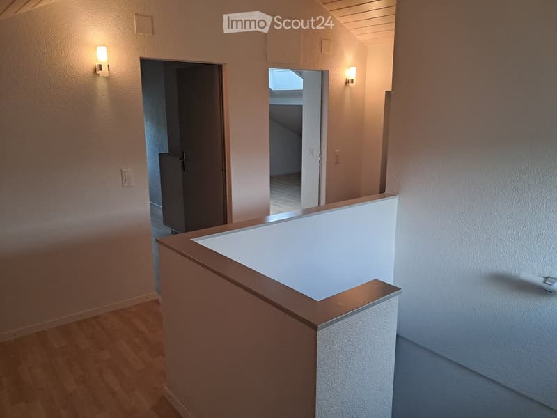 A modern hallway with wooden flooring, white walls, and built-in lighting. Features a staircase leading upwards and a closed door on the left side.