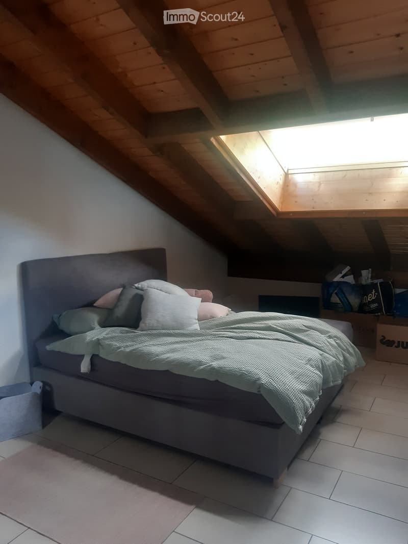 Cozy attic bedroom with wooden slanted ceilings, tiled floor, and a neatly made bed with pillows and a blanket.