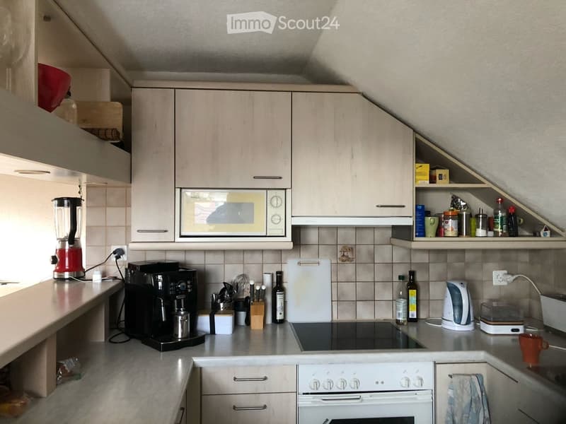 A modern kitchen with light-colored cabinets, a microwave, coffee maker, blender, and various kitchen appliances on the counter.