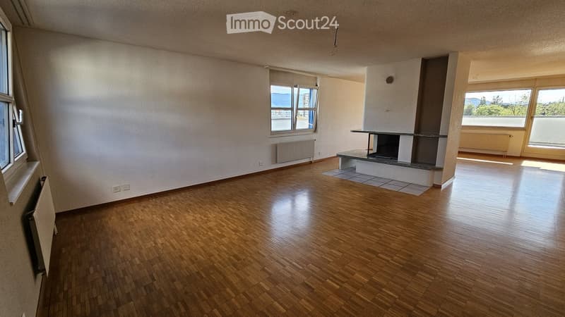 Empty room with wooden flooring, white walls, large windows, and a fireplace area.