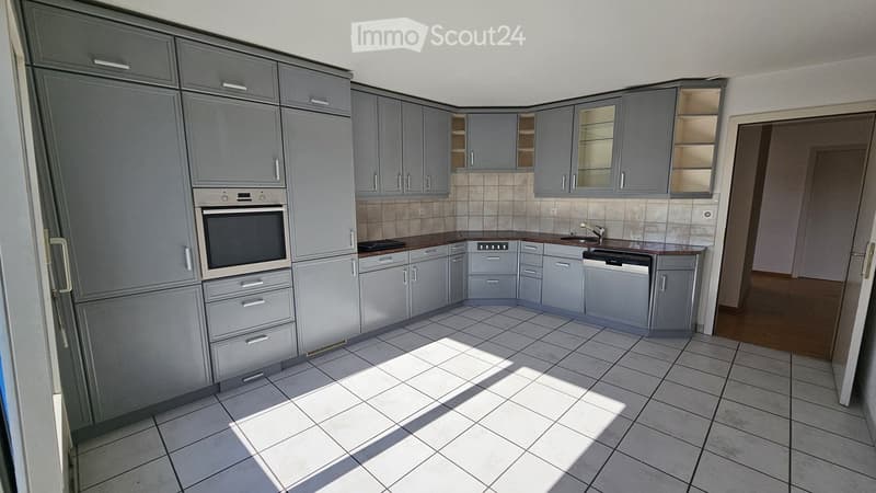 Modern kitchen with grey cabinets, white tiled floor, and stainless steel appliances including an oven and dishwasher.