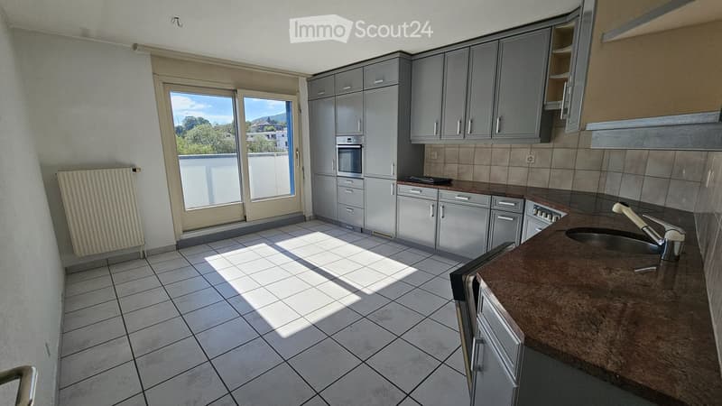 Modern kitchen with grey cabinets, tiled floor, and a large window offering a view of the outdoors.