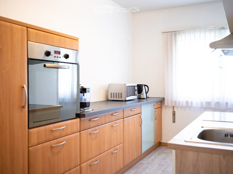Modern kitchen with wooden cabinets, stainless steel oven, microwave, coffee maker, kettle, and sink.