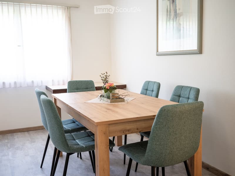 Dining room with a wooden table, six matching chairs, a vase with flowers, and a picture frame on the wall.