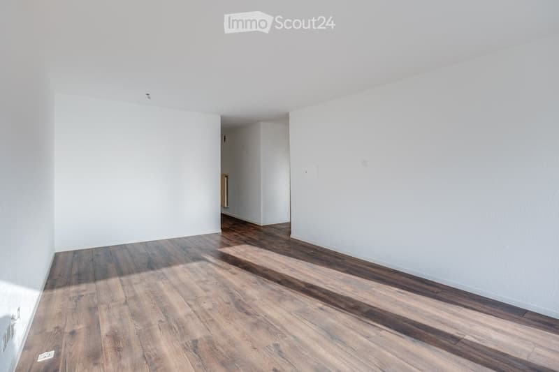 Empty room with white walls and wooden flooring, featuring a doorway leading to another room.