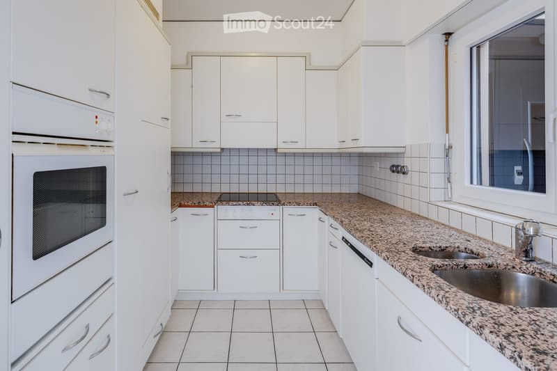 Modern white kitchen with granite countertop, dishwasher, built-in appliances, tiled floor, white cabinets, and an open window.