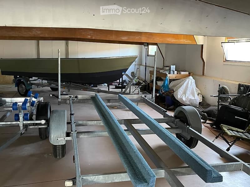 An unfurnished garage with a boat on a trailer, storage items, and a workbench.