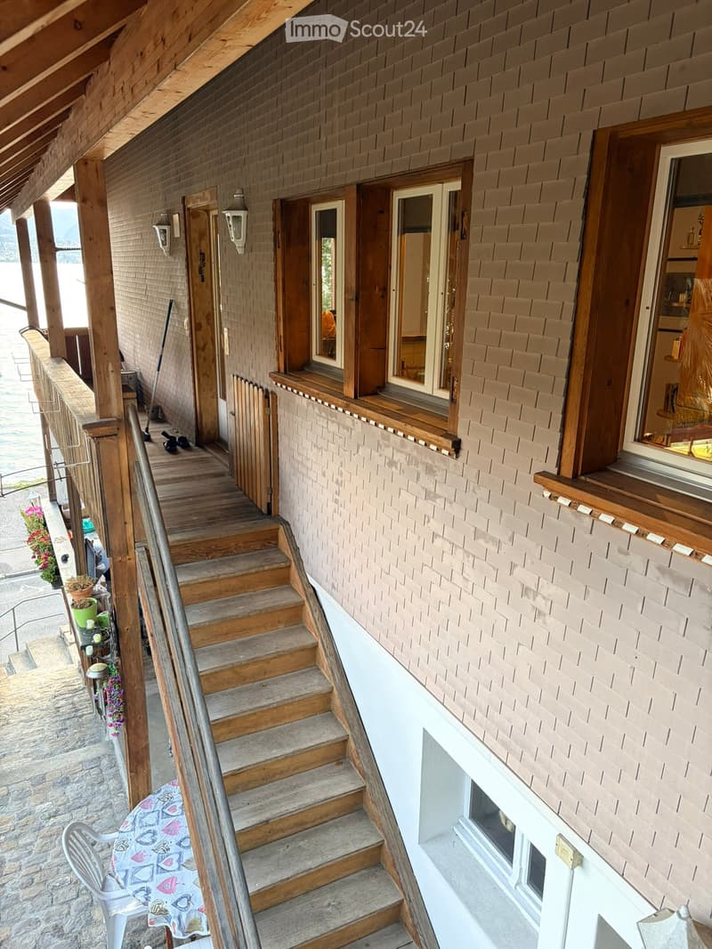 Wooden staircase leading up to a brick-walled balcony with wooden railings, small potted plants, and a view of the water.