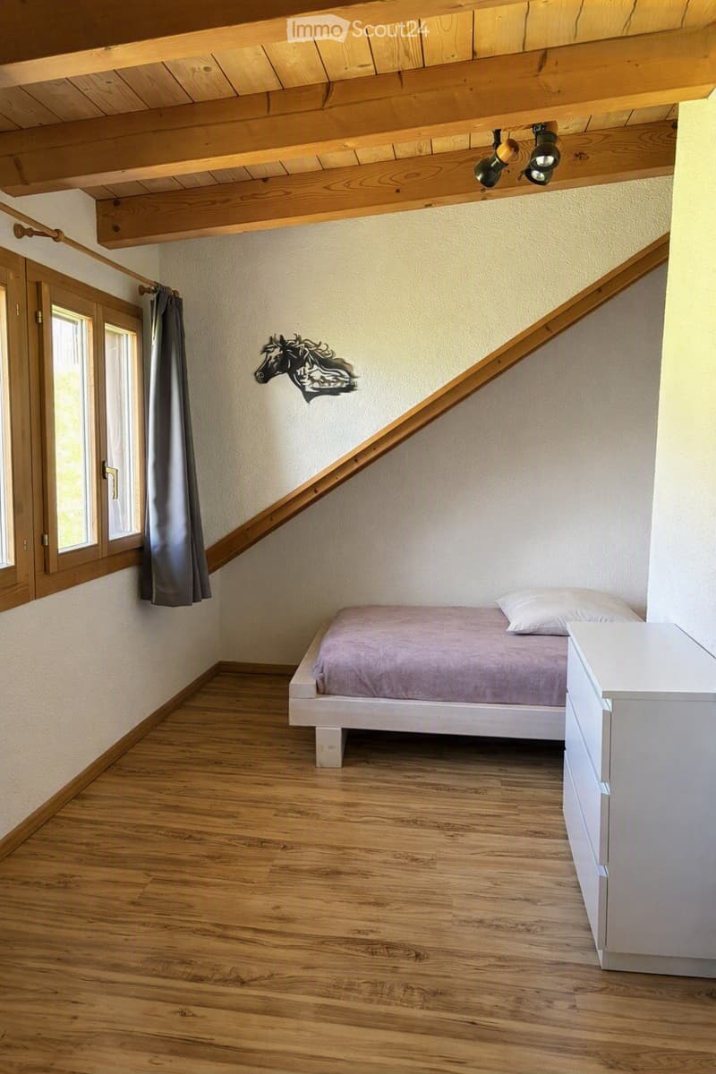 Cozy bedroom with wooden floor, slanted wooden ceiling, bed with grey bedding, nightstand, and a decorative horse wall art.