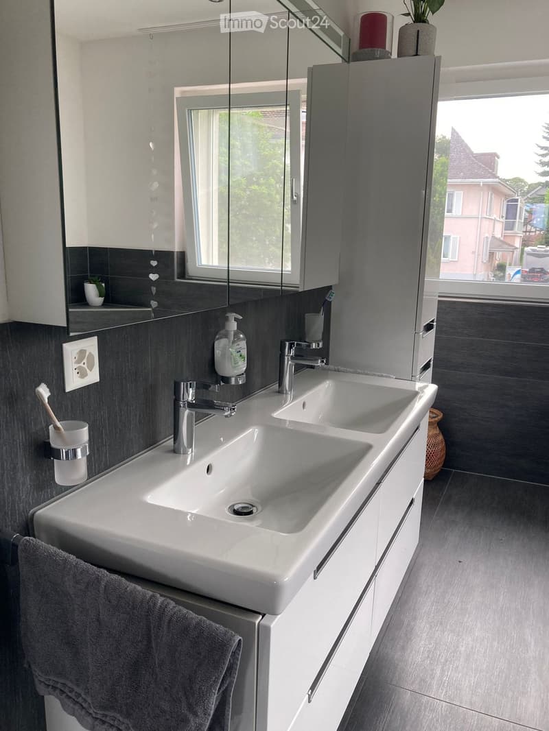 Modern bathroom with a double sink, sleek silver faucets, a large mirror with built-in cabinets, and a towel hanging on the side.