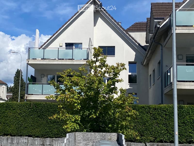 Modern two-story house with white exterior, multiple windows, and balconies with glass railings.