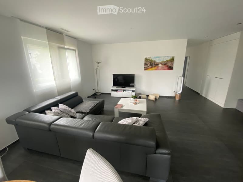 Modern living room with dark leather sofa, white coffee table, TV, floor lamp, and large windows with blinds.